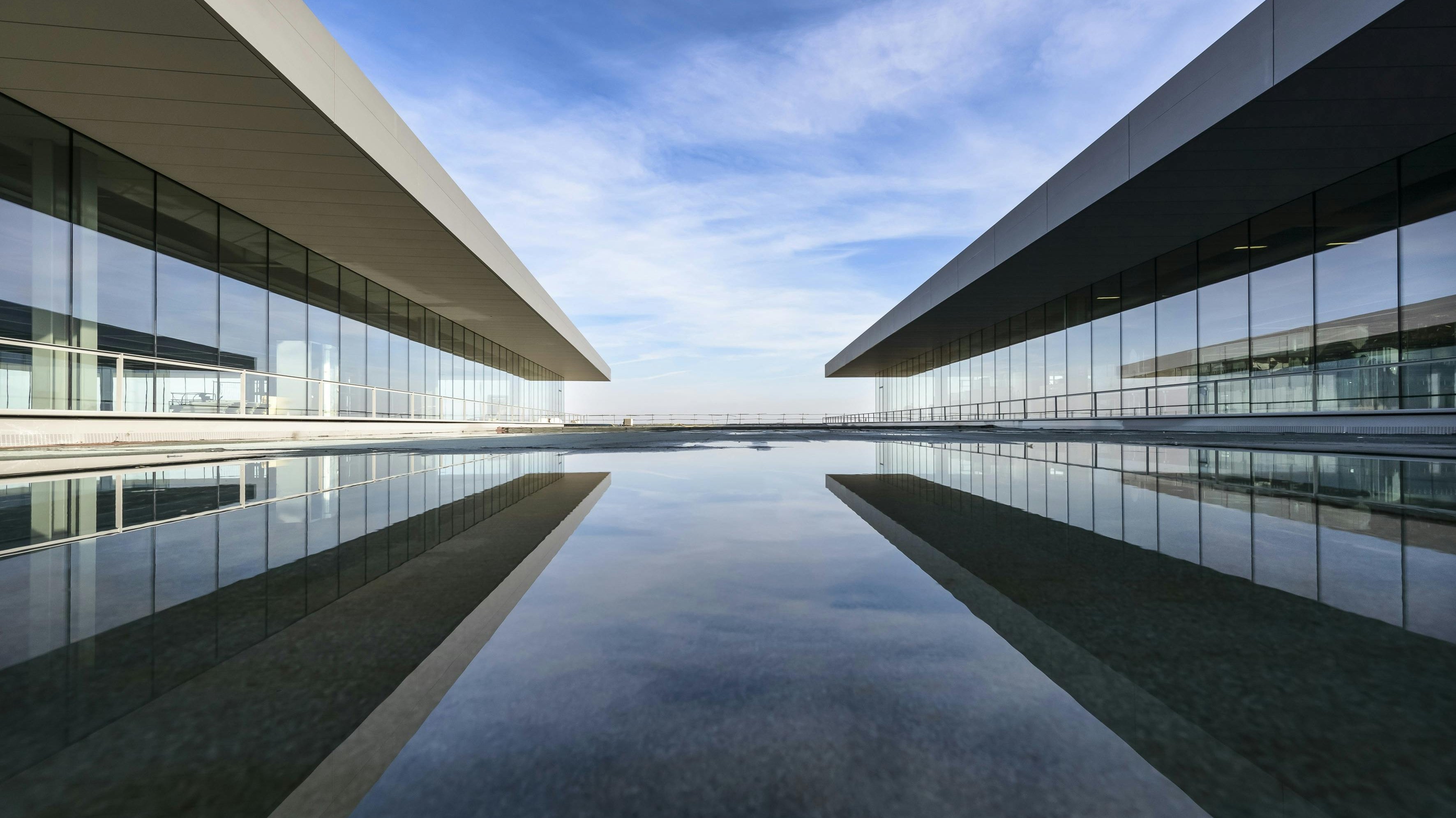 Twee moderne gebouwvleugels met grootformaat VSG-glasgevels spiegelen zich in een rustige wateroppervlakte en tonen het heldere, elegante effect van gelaagd veiligheidsglas in de architectuur.