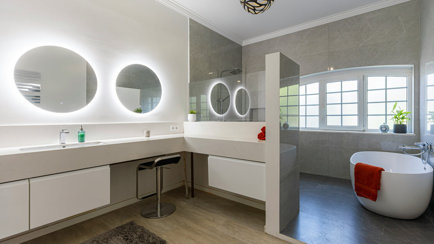 Helles, modernes Badezimmer mit zwei großen runden Badezimmerspiegeln mit LED-Beleuchtung, langer Waschtischfläche, separater Dusche und freistehender Badewanne – ideal zur Präsentation moderner beleuchteter Badspiegel.