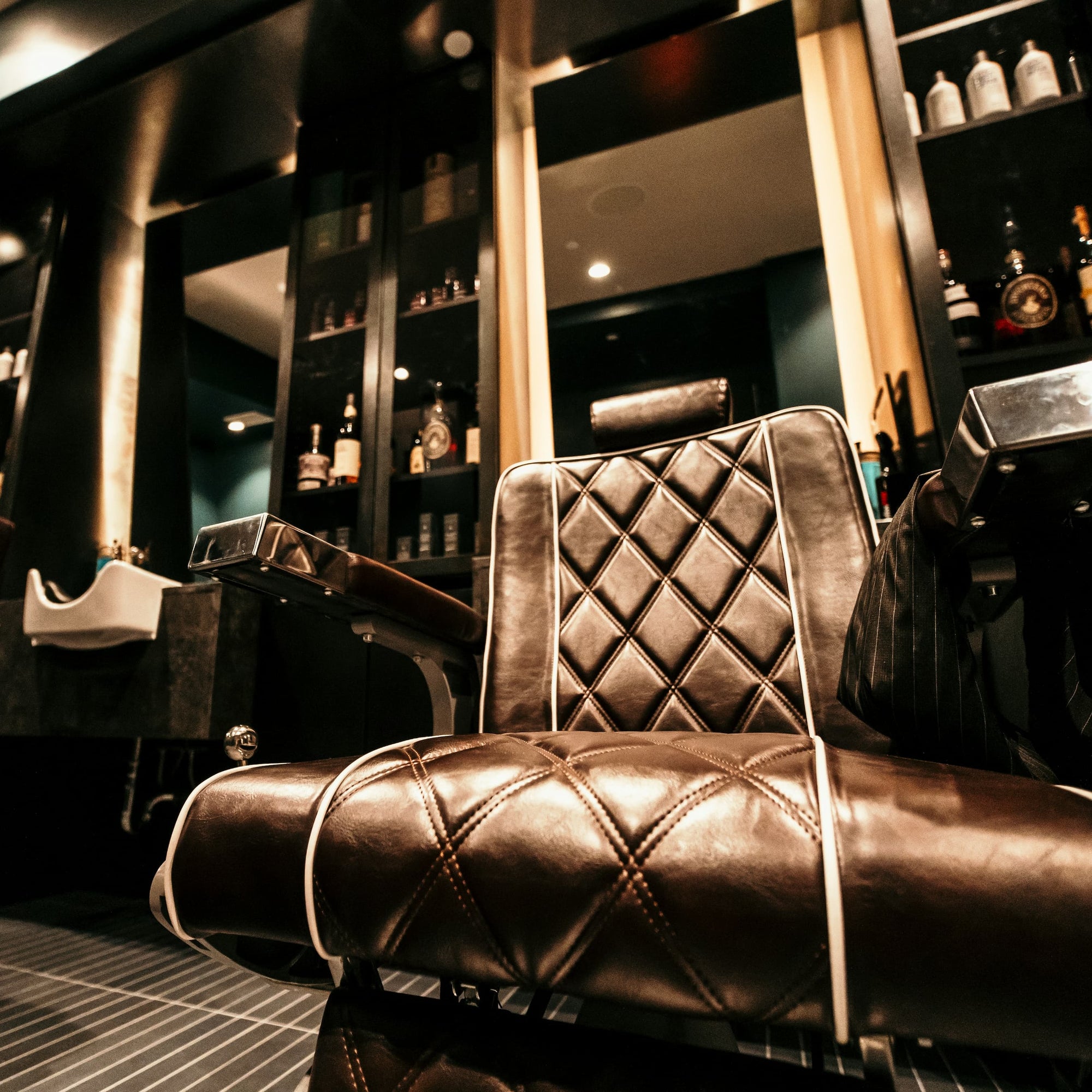 Großer Friseurspiegel mit integrierter Beleuchtung in einem eleganten Barbershop, im Vordergrund ein gepolsterter brauner Friseurstuhl und im Spiegelregal sichtbar platzierte Pflegeprodukte und Flaschen.