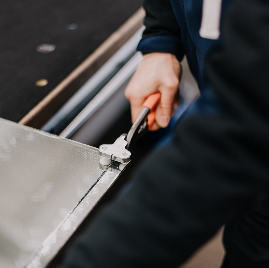 Hand schneidet Spiegelglas mit Brechzange entlang der Schnittkante – Manufakturarbeit bei Spiegelmax
