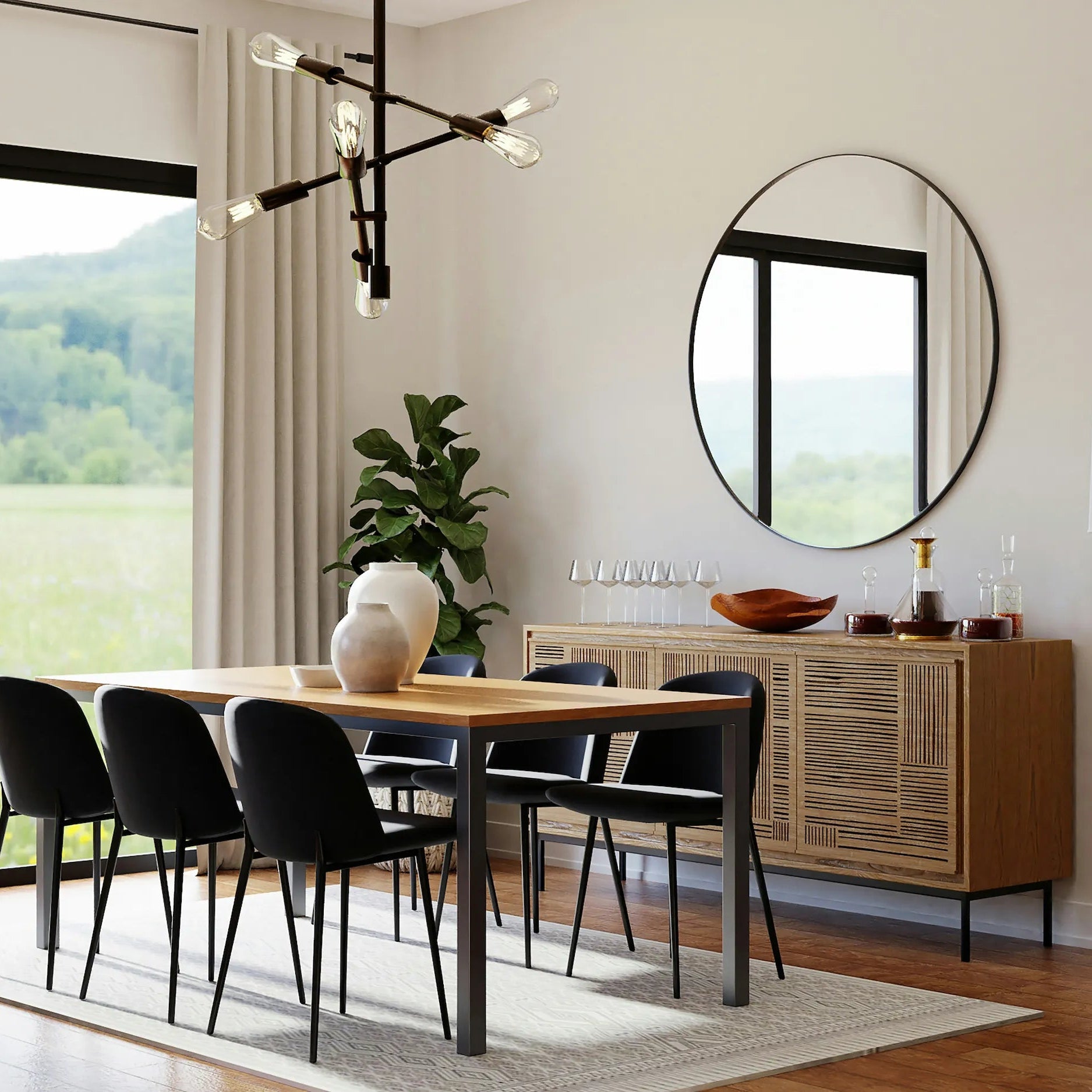 Modern eingerichtetes Esszimmer mit Holz-Esstisch, schwarzen Stühlen, großem runden Spiegel an der Wand, Sideboard aus Holz, dekorativen Vasen und Gläsern sowie einer großen Fensterfront mit Blick ins Grüne.