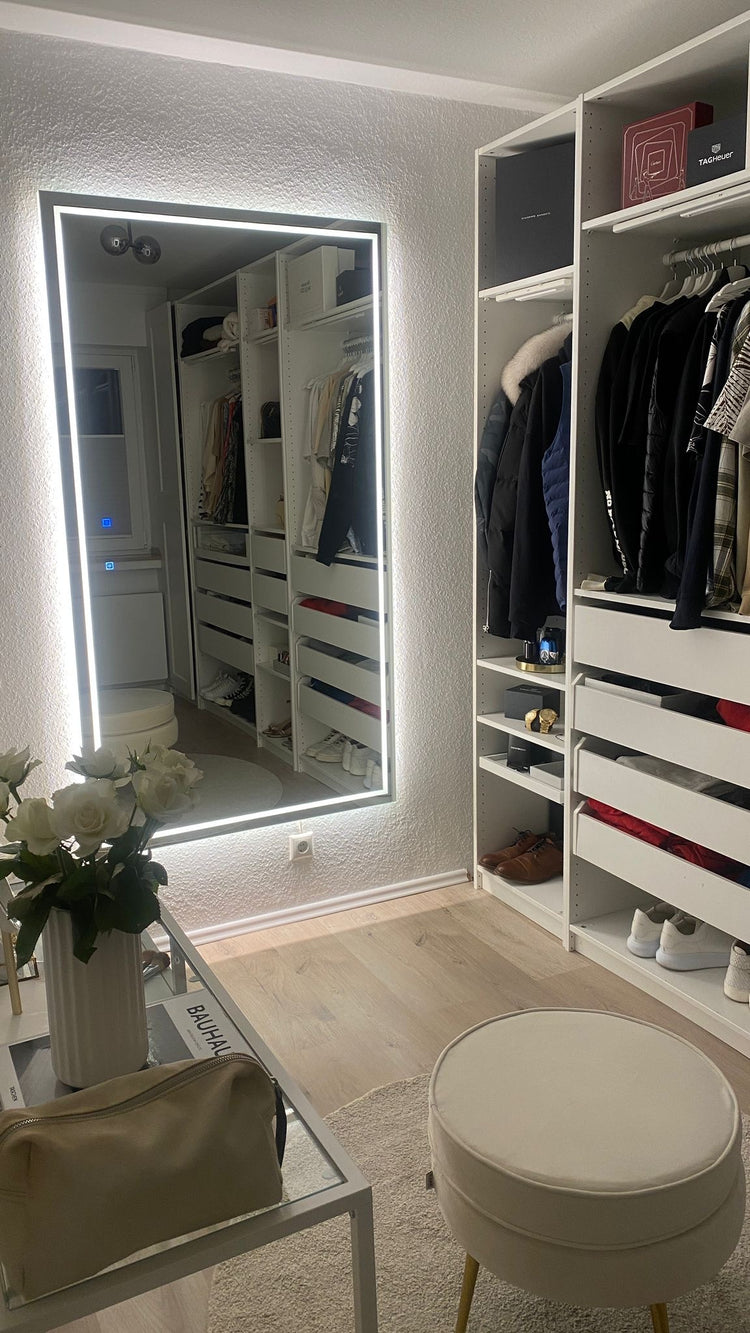 Begehbarer Kleiderschrank mit großem LED-Wandspiegel, offenen Regalen und Kleiderstangen.