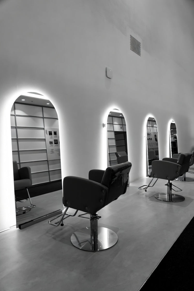 Moderner Friseursalon mit bogenförmigen Friseurspiegeln, heller LED-Hintergrundbeleuchtung und mehreren Stylingplätzen mit Salonstühlen