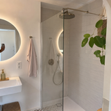 Walk-in-Duschwand aus Glas neben rundem Badspiegel