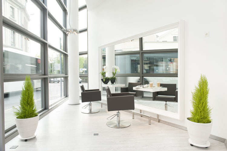Heller Friseursalon mit großem Wandspiegel, modernen Stylingstühlen, großen Fensterfronten und eleganter Salon-Einrichtung