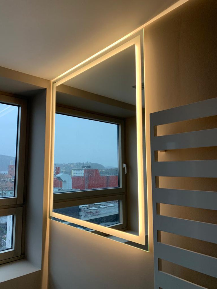 Rechteckiger LED-Badspiegel mit umlaufender warmweißer Beleuchtung in modernem Bad neben Fenster.