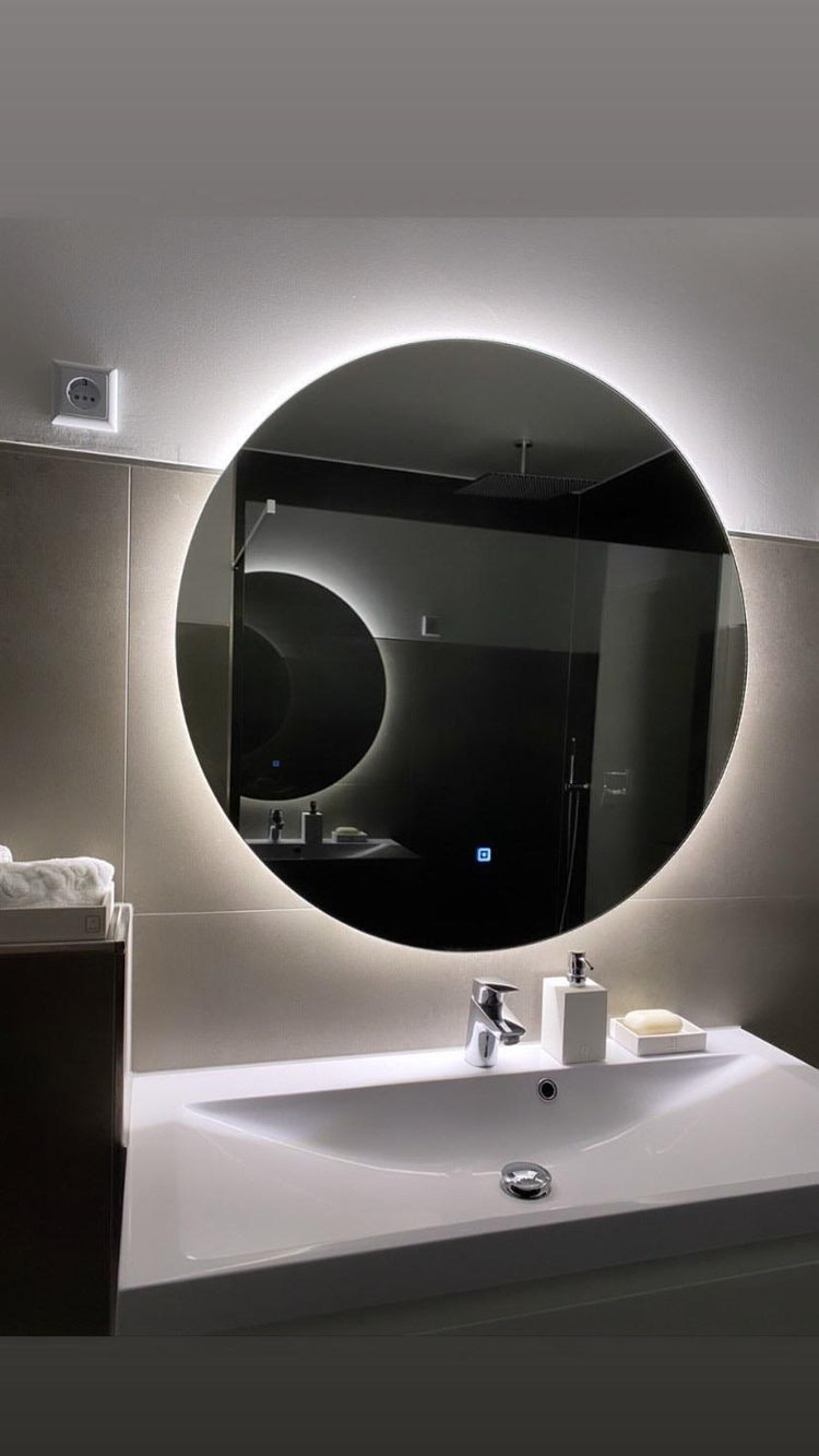 Runder Badspiegel mit umlaufender LED-Hinterleuchtung über weißem Waschbecken in modernem Badezimmer.