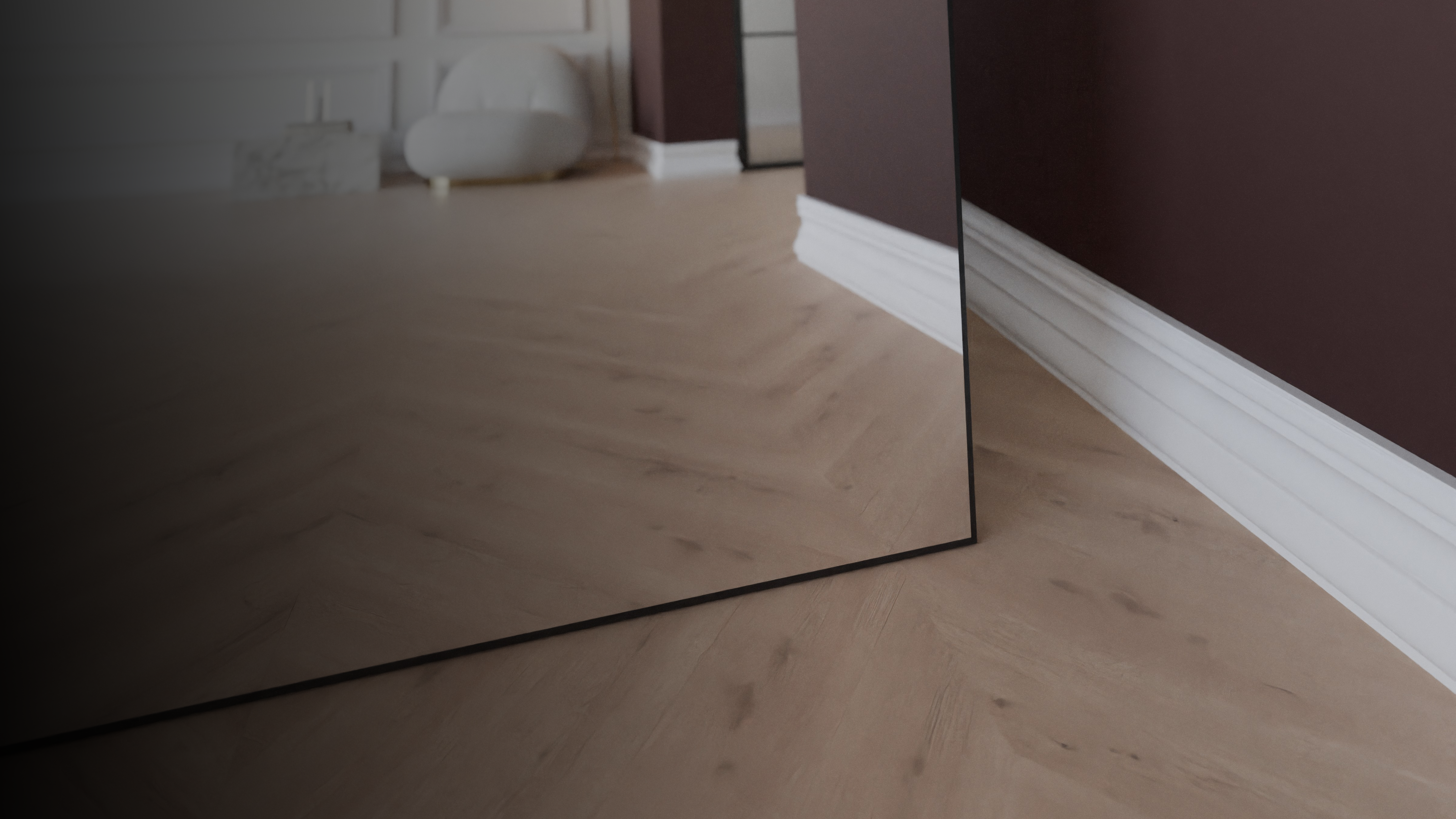 Detailaufnahme eines schwarzen Standspiegels auf hellem Holzboden vor bordeauxfarbener Wand mit weißer Sockelleiste.