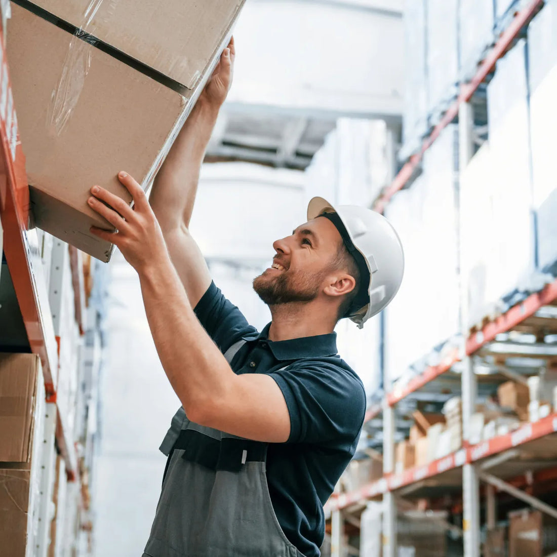 Ein Mitarbeiter im Lager hebt sorgsam ein Paket mit empfindlichen Möbeln oder Spiegeln für den Versand.