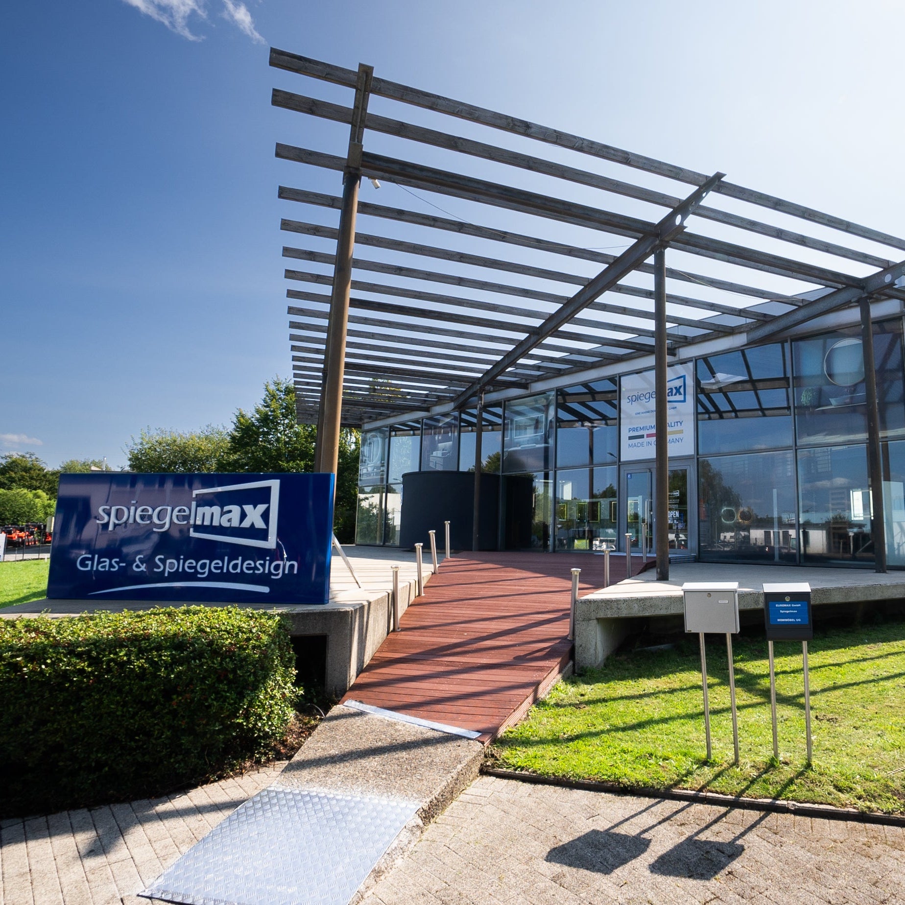 Spiegelmax Firmengebäude mit moderner Glasfassade und Außenbereich, inklusive Werbetafel für Glas- und Spiegeldesign